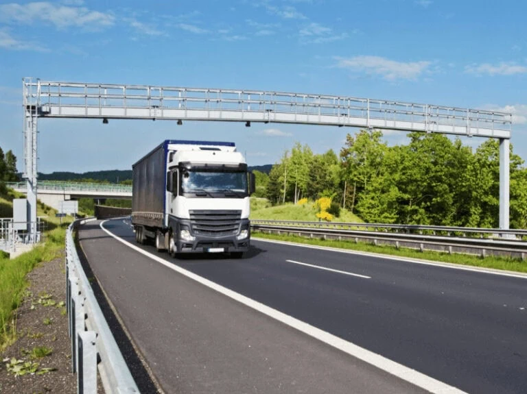 White truck passing under a toll gate, symbolizing toll fee payment in road transport