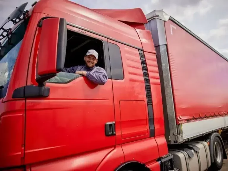 Smiling truck driver in red truck looking out the window, representing road transport