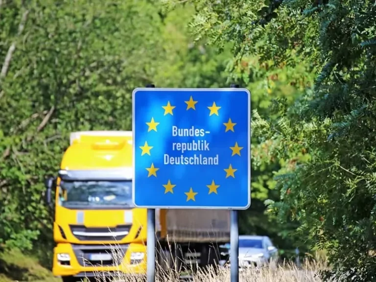 A truck is approaching the German border, passing by road signs indicating entry into Germany